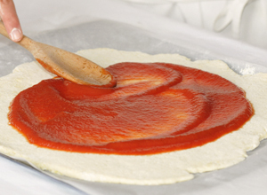 Etaler le coulis de tomate sur la pâte à pizza sans gluten